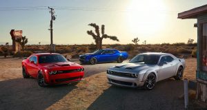 Red, white, and blue Dodge Challengers parked in front of a sunset at an abandoned gas station in the West.