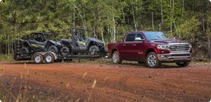 Red 2021 Ram 1500 truck towing a heavy load of ATVs on a dirt road.