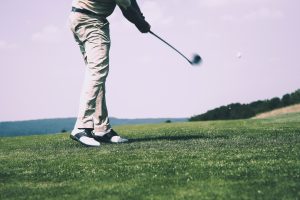 Image of a man in a white golfing outfit hitting the golf ball on the golf course on a sunny day.