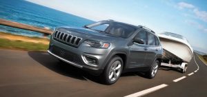 A Jeep Cherokee with a boat in tow driving along a sea-side cliff.