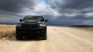 Black Jeep Grand Cherokee driving along a desert road with stormy clouds ahead.