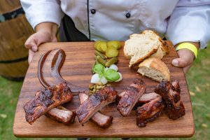 Close-up image of a serving holding a wooden board of breads and barbecue meats.