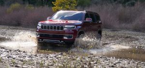 Red 2022 Jeep Wagoneer driving through a puddle of water .