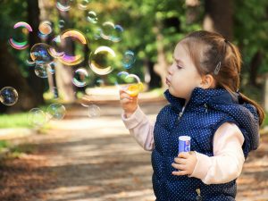 Little girl in blue vest blowing bubbles in the park.