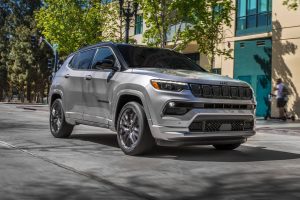 A gray 2022 Jeep Compass parked outside of a shop downtown in the shade.