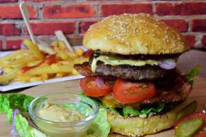 Up close image of a cheeseburger with fries and ketchup with a side of mayo on a cutting board.